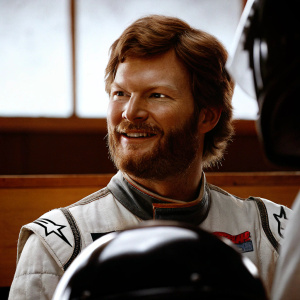 Dale Earnhardt Jr., bearded racer, casual smile. Racing gear, team logos prominent. Indoor event, blurred backdrop. High-res close-up.