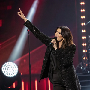 Laura Pausini performing at the Grammy Awards, dramatic lighting, black sequined jacket, dynamic pose, spotlight