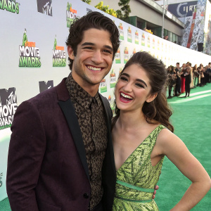 Tyler Posey and Seana Gorlick, smiling brightly, at MTV Movie Awards. Green carpet with logos
