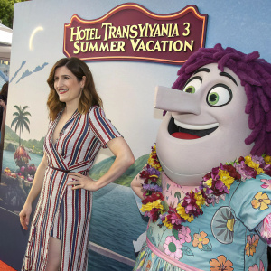 Kathryn Hahn in promotional shot for 'Hotel Transylvania 3: Summer Vacation'. Beside large animated character. Striped dress. Colorful movie-themed backdrop.