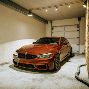 A hyper-realistic 3D model of a BMW M4 CS. Red car parked in a dimly lit garage. Only a few lights casting shadows on the polished surface.