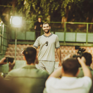 Karim Benzema, wearing jersey number 9, posing for fans. Faint blur of audience and cameras in the background.