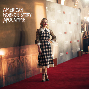 Leslie Grossman at the Hollywood premiere of 'American Horror Story: Apocalypse'. She stands confidently on a red carpet event. Wearing a sophisticated black and white checkered dress with a delicate lace collar. The backdrop features illuminated studio logos and branding.