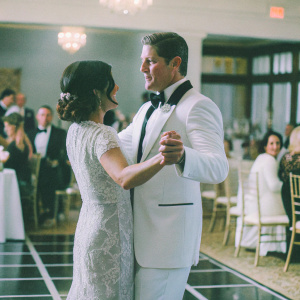 Sean Kanan and Athena Ubach attending a gala event. Sean wears a classic tuxedo, Athena in an elegant lace dress. Crowded ballroom setting with chandeliers