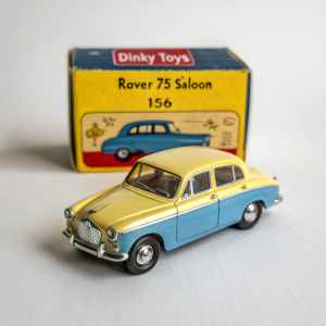 Vintage Dinky Toys Rover 75 Saloon car model 156, showcasing its yellow and blue hues. The model is placed on the original packaging, which bears the Dinky Toys logo and model number. The box exhibits a classic design.