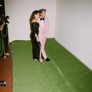 Mädchen Amick and Derek Warburton at a glamorous award show. Amick wears a black sequined dress, Warburton in a tuxedo. Red carpet with flashing cameras.