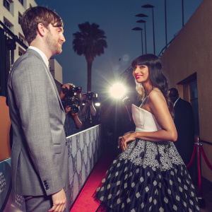 James Blake and Jameela Jamil attending the Critics' Choice Awards. James in a grey suit, Jameela in a black and white gown. Red carpet setting.