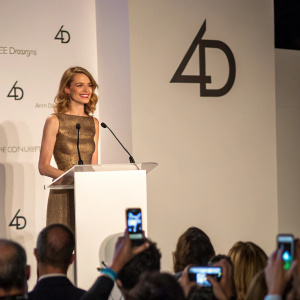 Natalia Vodianova speaking at a charity gala, standing at a podium with F4D logo behind her. Audience members are taking photos.