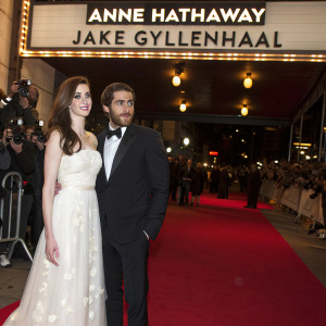 Photo of Anne Hathaway and Jake Gyllenhaal at a gala event. They stand beside a large banner advertising an upcoming film festival. Red carpet, flashbulbs, and a crowd of paparazzi