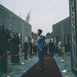 Alphonso Davies, in a blue suit, at the FIFA Awards Ceremony. Red carpet, flashing cameras, elegant backdrop.