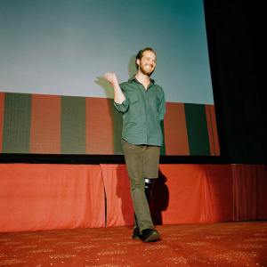 Nick Vujicic, bearded and smiling, center stage at TED Talks. Dynamic, multicolored backdrop.