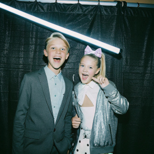 JoJo Siwa and Carson Lueders at the Nickelodeon HALO Awards. They are posing against a black backdrop with the bright, vibrant Nickelodeon logo.