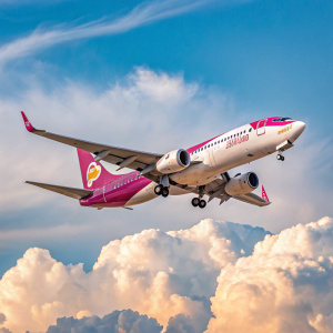 A NokAir Boeing 737-400 in a stunning pink and white livery soaring through a clear blue sky, with fluffy clouds in the background.