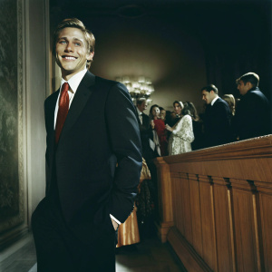 Charlie Hunnam at a glamorous gala, wearing a dark suit and red tie. Smiling confidently in front of a crowd.