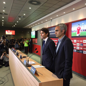 Jose Mourinho and Aitor Karanka, in formal suits, during a press conference. The backdrop features large screens and standing microphones. Event is held indoors, media and spectators in the background.