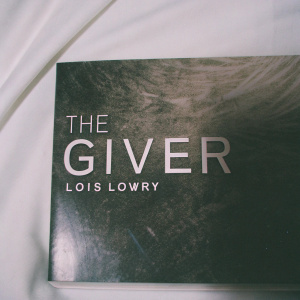 Book cover design for 'The Giver' by Lois Lowry. Black and white image with sleek modern typography. Quote on right side. Close-up view focusing on text and graphic elements. White background.