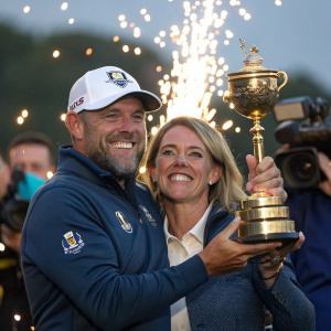 Lee Westwood and Helen Storey grinning as they hold a sparkling trophy. Surrounded by cheers and flashing cameras.