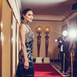 Gal Gadot, star of Wonder Woman, in elegant black dress with intricate beading, posing on the red carpet at the Golden Globes. Luxurious backdrop with Globe statues and flashing cameras