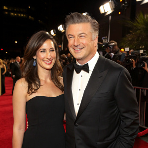 Alec Baldwin and Nicole Seidel at the Hollywood Awards. Wearing black tuxedos and smiling. Red carpet scene with flashing cameras.