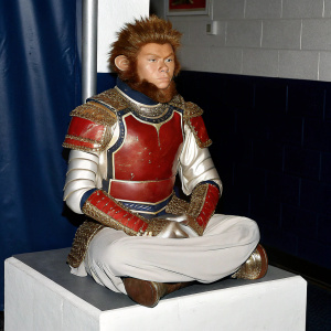 Statue of Sun Wukong, the Monkey King, standing in a meditative pose. Detailed armor with red and gold accents. Spiky hair. Displayed in a dark room with minimal lighting.
