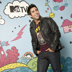Colby O'Donis, sporting a vibrant outfit including a graphic t-shirt, leather jacket, and dark jeans, grins confidently. Set against a whimsical backdrop featuring cartoonish elements and the MTV logo.