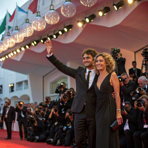 Riccardo Scamarcio and Valeria Golino at Venice Film Festival. Festive atmosphere with numerous cameras and flashing lights.