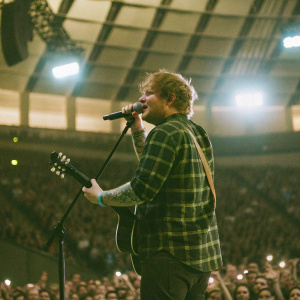 Ed Sheeran, performing live at the O2 Arena. Dressed in a green plaid shirt. Blue stage lights