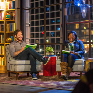 Ike Barinholtz and Mindy Kaling at a cozy book signing event, surrounded by shelves of books and a patterned rug.