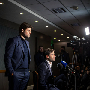 Mauricio Pochettino and Jesus Perez, coaches of Tottenham Hotspur, inside a dimly lit press conference room.