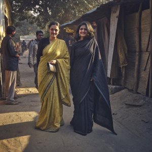 Dia Mirza and Zoya Akhtar at the book fair. Dia Mirza donning a yellow sari. Zoya Akhtar in a black saree. Both are Indian, smiling for the camera. Outdoors, sunny day.