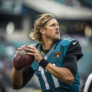 Blaine Gabbert, intense focus, wearing a Jacksonville Jaguars jersey with number 11. About to throw a football. The stadium background is blurred