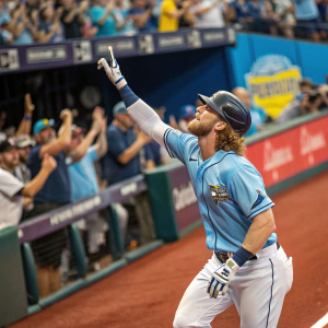 Brett Phillips in action at the stadium. Wearing a light blue jersey, white pants, batting helmet, and gloves. Surrounded by cheering fans.