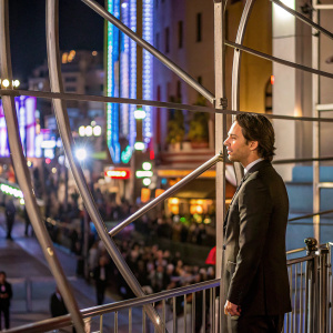 Zach Braff at the premiere event. Wearing a black suit, standing in front of a crowded street with bright lights.