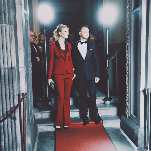 Natalie Dormer, in a bold red suit, and Anthony Byrne, in a sharp black tuxedo, pose at the GQ Men of the Year Awards. Red carpet ambiance