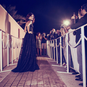Maisie Williams, attending a film festival. Wearing a long black dress with intricate detailing. Dark outdoor setting with crowd of fans.