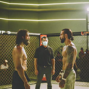 Rob Font and Marlon Vera, shirtless MMA fighters, facing off at UFC Apex. The referee in a black shirt separates them. UFC branding visible on the ring's backdrop. Live event photograph.