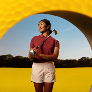 Hana Wakimoto, Asian golfer, in vibrant red polo shirt and white shorts, on a sunny golf course.