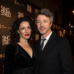 Camille O'Sullivan and Aidan Gillen attending the opening night of Sing Street. Both dressed formally. Dark and moody setting with event logos in the background.