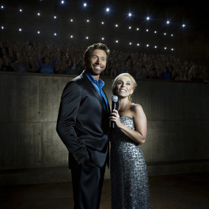 Hugh Jackman and Lady Gaga at a high-profile awards show. Both are dressed to impress. Jackman in a tailored black suit, Lady Gaga in a sparkling silver gown. Crowds cheering in the background.