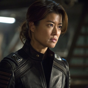 Lt. Sharon 'Boomer' Valerii, played by Grace Park, in an intense scene from Battlestar Galactica. Wearing a black leather-like jacket with futuristic details. Dimly lit, focusing on her focused expression. Background blurred, lighting casting shadows on jacket.
