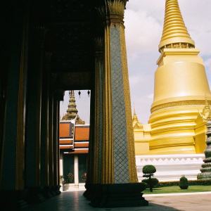 The majestic Grand Palace of Bangkok, a testament to bygone opulence, stands illuminated. Its gilded spires, adorned with intricate blue and vibrant color patterns, rise against the sky. Pillars and ornate details narrate the grandeur of a past era.