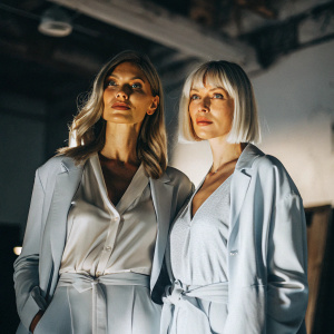 Carol Alt and Nadja Auermann, both women with striking features, posing in a dimly lit studio setting.