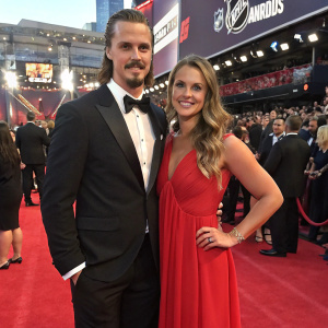 Erik Karlsson and Melinda Currey at the 2017 NHL Awards ceremony. Erik in a black tuxedo. Melinda in a flowing red dress. Crowded backdrop