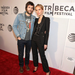 Jim Sturgess and Isabel Lucas at the Tribeca Film Festival premiere. Jim in denim jacket over a graphic t-shirt. Isabel in a tailored black blazer with chic hairstyle. Backdrop features repeated festival logos and text. They stand on a textured red carpet.