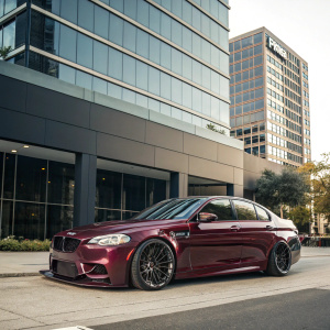 High-end luxury car, BMW M5 in glossy maroon, parked outside modern office building. Detailed shot showcasing sleek lines and powerful presence. Photographic masterpiece capturing elegance and performance.