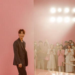 Kim Young-Kwang, South Korean actor, at a fashion event. Dark suit, smiling confidently. Crowded venue, bright lights