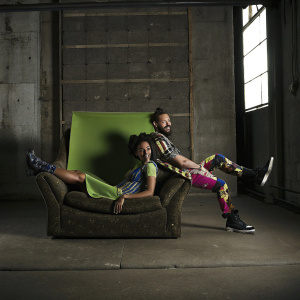 Kyla Pratt and Danny Kirkpatrick in vibrant attire. Green screen backdrop, dynamic angles. Artistic photo shoot.