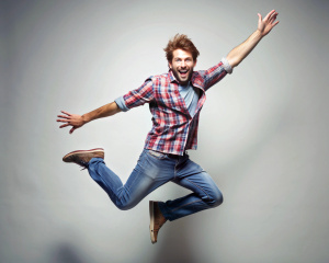 Un hombre saltando feliz, con ropa informal, joven, entre 25 y 30 años, jovial y sonriente. 
