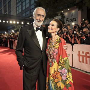 Sir Christopher Lee and Birgit Kroencke, both elegantly dressed, are seen at the Toronto International Film Festival. Lee in a black suit, Kroencke in a vibrant, floral print dress. They pose confidently on a bustling red carpet surrounded by flashing cameras and enthusiastic fans.
