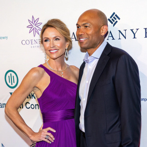 Mariano Rivera and Amy Robach at a charity gala. Amy in a vibrant purple gown. Mariano with a bald head and formal shirt. White backdrop with company logos